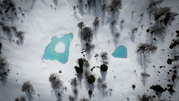 Aerial view of turquoise waters piercing through the stark white snow amidst the scattered trees of Mount Colmet Arpy Valle d Aosta Italy. Aerial view of turquoise waters piercing through the stark white snow amidst the scattered trees of Mount Colmet Arpy Valle d Aosta Italy.
