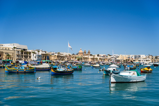 View of traditional colorful Maltese fishing boats called luzzu floating on the calm blue water of the harbor under a clear sky in Marsaskala Southern Region Malta. View of traditional colorful Maltese fishing boats called luzzu floating on the calm blue water of the harbor under a clear sky in Marsaskala Southern Region Malta.