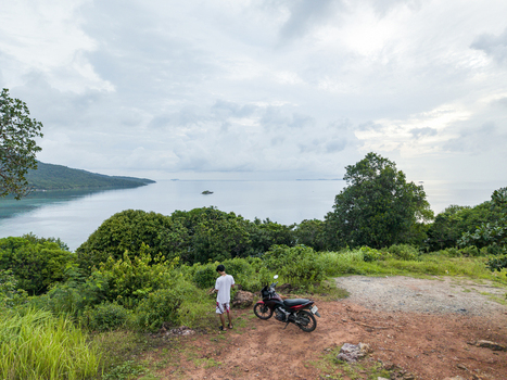 Aerial view of a lone figure stands beside a parked motorcycle gazing out at the tranquil sea near Cottage Legon Waru Karimunjawa Central Java Indonesia.