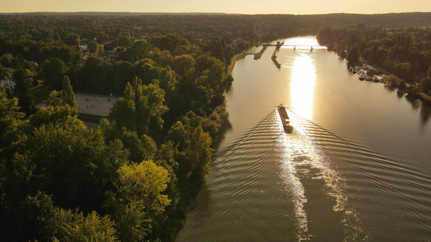 Aerial view of a barge navigating the Seine river during golden hour surrounded by lush green forests and trees in Chartrettes Ile de France France. Aerial view of a barge navigating the Seine river during golden hour surrounded by lush green forests and trees in Chartrettes Ile de France France.