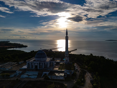 Aerial view of the Sultan Haji Fisabilillah Mosque with its tall minaret and blue dome overlooking the sea at sunset Tanjung Pinang Riau Islands Indonesia. Aerial view of the Sultan Haji Fisabilillah Mosque with its tall minaret and blue dome overlooking the sea at sunset Tanjung Pinang Riau Islands Indonesia.