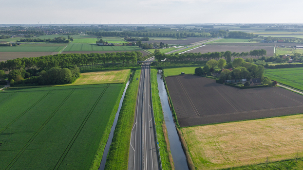 Aerial view of a straight highway passing through lush green agricultural fields and canals under a clear sky in Vierpolders South Holland Netherlands. Aerial view of a straight highway passing through lush green agricultural fields and canals under a clear sky in Vierpolders South Holland Netherlands.