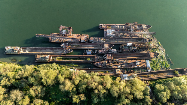 Aerial view of a collection of industrial barges and cargo ships moored along the riverbank surrounded by lush green trees in Sremska Mitrovica Vojvodina Serbia.