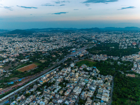 Aerial view of the cityscape of Udaipur featuring dense urban development a railway line and surrounding lush greenery under a soft twilight sky Udaipur Rajasthan India.