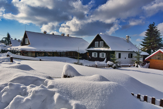View of snow covered cottages nestled in a winter wonderland under a bright blue sky dotted with fluffy clouds Donovaly Banskobystricky kraj Slovakia. View of snow covered cottages nestled in a winter wonderland under a bright blue sky dotted with fluffy clouds Donovaly Banskobystricky kraj Slovakia.