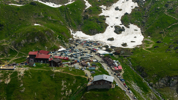 Aerial view of the Transfagarasan mountain pass with parked cars mountain lodges and patches of snow on the green slopes in Curtea de Arges Arges County Romania.