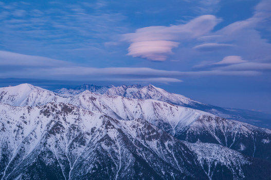 Aerial view of the snow capped peaks of the High Tatras mountains under a sky filled with unique lenticular clouds in Vysoke Tatry Presov Region Slovakia.
