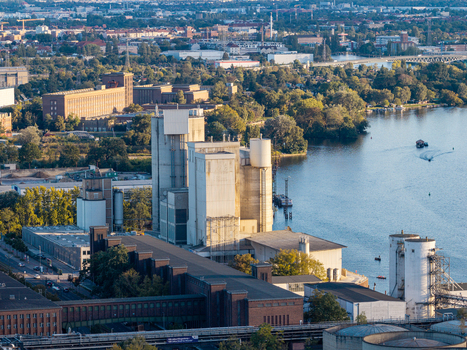 Aerial view of the Zementwerk Berlin concrete plant situated along the riverbank with industrial silos surrounding urban landscape and lush greenery in Berlin Berlin Germany. Aerial view of the Zementwerk Berlin concrete plant situated along the riverbank with industrial silos surrounding urban landscape and lush greenery in Berlin Berlin Germany.