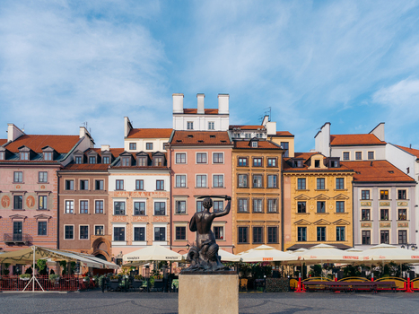 View of the Warsaw Mermaid statue in the historic Old Town Market Square surrounded by colorful traditional townhouses and outdoor cafe umbrellas in Warsaw Masovian Voivodeship Poland. View of the Warsaw Mermaid statue in the historic Old Town Market Square surrounded by colorful traditional townhouses and outdoor cafe umbrellas in Warsaw Masovian Voivodeship Poland.