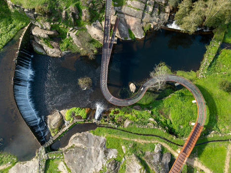 Aerial view of Acude da Ribeira featuring a modern metal walkway curving over the river and rocky landscape in Ervedal Coimbra Portugal. Aerial view of Acude da Ribeira featuring a modern metal walkway curving over the river and rocky landscape in Ervedal Coimbra Portugal.