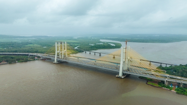 Aerial view of the modern cable stayed Zuari Bridge spanning the river with lush green banks and a cloudy sky in Cortalim Goa India.