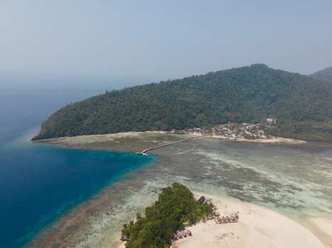 Aerial view of Yenbuba village with a long wooden jetty extending into turquoise coral reef waters surrounded by lush tropical hills in Raja Ampat Southwest Papua Indonesia. Aerial view of Yenbuba village with a long wooden jetty extending into turquoise coral reef waters surrounded by lush tropical hills in Raja Ampat Southwest Papua Indonesia.