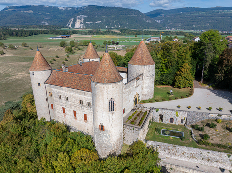 Aerial view of Champvent Castle with its stone towers and terracotta roofs surrounded by lush trees and rolling hills in the countryside of Champvent Vaud Switzerland. Aerial view of Champvent Castle with its stone towers and terracotta roofs surrounded by lush trees and rolling hills in the countryside of Champvent Vaud Switzerland.