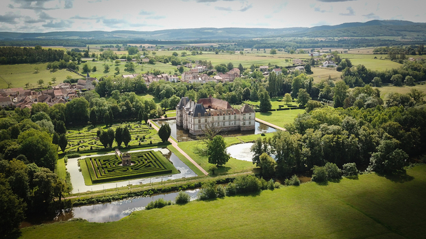 Aerial view of Chateau de Cormatin with its moat and formal labyrinth gardens surrounded by lush greenery and the village Cormatin Bourgogne Franche Comte France. Aerial view of Chateau de Cormatin with its moat and formal labyrinth gardens surrounded by lush greenery and the village Cormatin Bourgogne Franche Comte France.