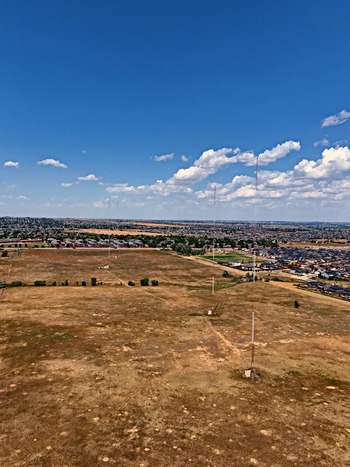 Aerial view of radio towers standing in a dry grassy field with suburban residential neighborhoods in the background under a clear blue sky in Thornton Colorado United States. Aerial view of radio towers standing in a dry grassy field with suburban residential neighborhoods in the background under a clear blue sky in Thornton Colorado United States.
