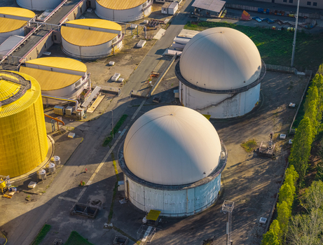 Aerial view of large white spherical biogas storage domes and yellow cylindrical tanks at an industrial wastewater treatment facility with paved paths and surrounding trees in Italy. Aerial view of large white spherical biogas storage domes and yellow cylindrical tanks at an industrial wastewater treatment facility with paved paths and surrounding trees in Italy.