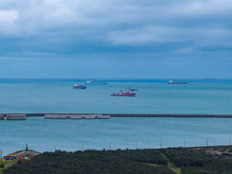 Aerial view of cargo ships and a support vessel navigating the turquoise sea near the breakwater under a cloudy sky in Taichung Taichung City Taiwan. Aerial view of cargo ships and a support vessel navigating the turquoise sea near the breakwater under a cloudy sky in Taichung Taichung City Taiwan.