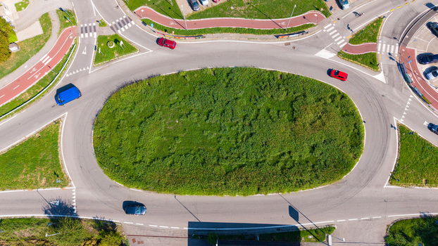 Aerial view of a traffic roundabout with cars driving on the asphalt road surrounding a central grassy island in Milan Lombardy Italy.