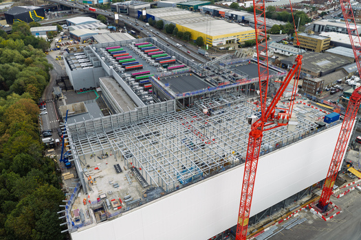 Aerial view of a data center construction site with steel framework red cranes and colorful cooling units on the roof United Kingdom.