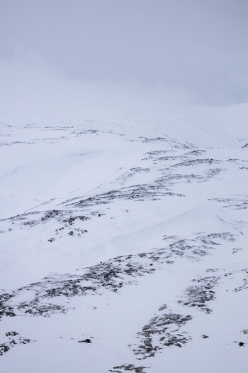 View of snow covered mountain slopes with dark rocky outcrops under a heavy overcast winter sky Kvaloya Troms Norway.