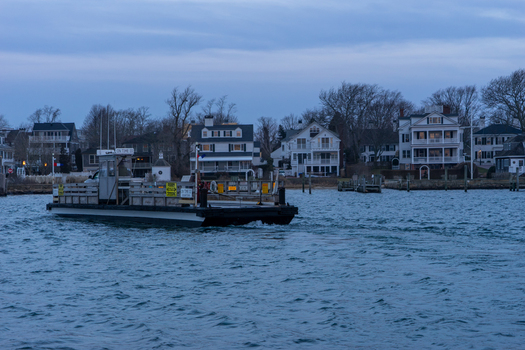 View of the On Time ferry crossing the harbor towards historic coastal houses and waterfront properties at twilight in Edgartown Massachusetts United States.