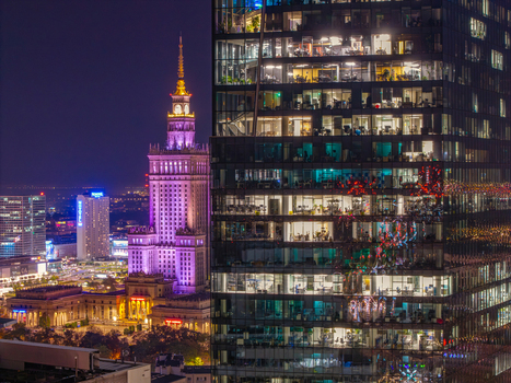 Aerial view of the Palace of Culture and Science illuminated in purple next to a modern glass skyscraper with glowing office windows at night in Warsaw Poland. Aerial view of the Palace of Culture and Science illuminated in purple next to a modern glass skyscraper with glowing office windows at night in Warsaw Poland.