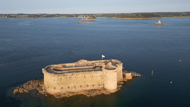 Aerial view of the imposing Ch&acirc;teau du Taureau a medieval fortress rising defiantly from the dark blue sea its weathered stone warmed by the golden sunlight Plouezoc h Bretagne France.