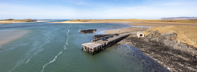 Aerial view of Ballyness Bay featuring a concrete pier extending into the water with parked cars surrounded by sandy beaches dunes and rocky coastline in Ballyness County Donegal Ireland. Aerial view of Ballyness Bay featuring a concrete pier extending into the water with parked cars surrounded by sandy beaches dunes and rocky coastline in Ballyness County Donegal Ireland.