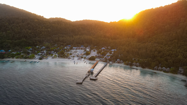 Aerial view of Raja Ampat featuring a wooden pier lush tropical hills and a sandy beach at sunset in Raja Ampat Southwest Papua Indonesia.