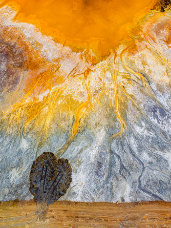 Aerial view of vibrant orange and yellow mineral rich sediment flowing through grey soil with a dark textured mound at a mining site in Andalusia Spain. Aerial view of vibrant orange and yellow mineral rich sediment flowing through grey soil with a dark textured mound at a mining site in Andalusia Spain.