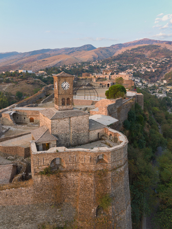 Aerial view of Gjirokaster Fortress with its iconic clock tower and historic stone walls set against the mountainous landscape of Gjirokaster Gjirokaster County Albania. Aerial view of Gjirokaster Fortress with its iconic clock tower and historic stone walls set against the mountainous landscape of Gjirokaster Gjirokaster County Albania.