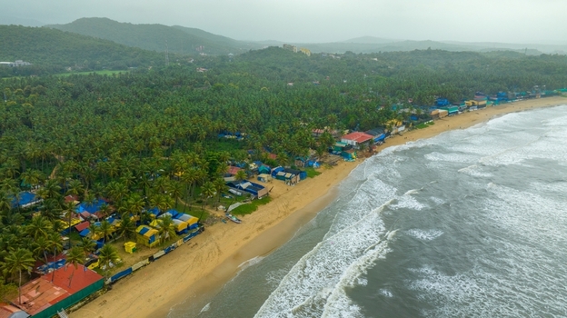 Aerial view of Palolem Beach with lush palm trees colorful beach huts and waves crashing on the sandy shore in Canacona Goa India.