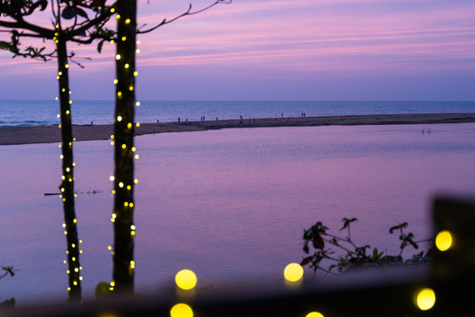 View of a serene coastal lagoon at twilight with people walking on a sandbar and fairy lights in the foreground Galle Southern Province Sri Lanka.