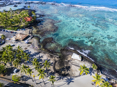 Aerial view of Kahalu u Beach Park featuring turquoise waters coral reefs and palm trees with people on the shore in Kailua Kona Hawaii United States. Aerial view of Kahalu u Beach Park featuring turquoise waters coral reefs and palm trees with people on the shore in Kailua Kona Hawaii United States.
