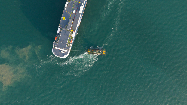 Aerial view of a large cargo ship being assisted by a tugboat in turquoise waters near the port of Laem Chabang Chon Buri Thailand.