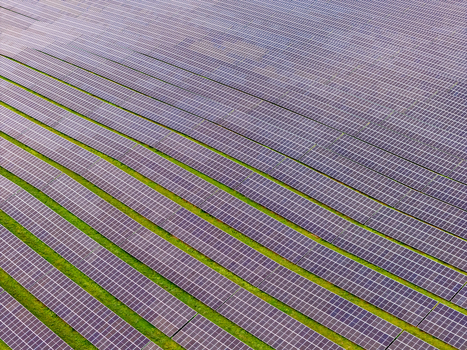 Aerial view of rows of solar panels in a large solar farm with green grass strips between them in Poland.