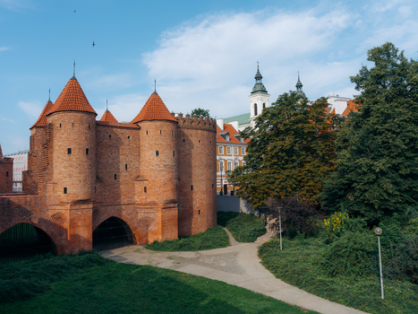 View of the historic Warsaw Barbican with its red brick towers and fortifications surrounded by lush greenery and trees in Warsaw Masovian Voivodeship Poland. View of the historic Warsaw Barbican with its red brick towers and fortifications surrounded by lush greenery and trees in Warsaw Masovian Voivodeship Poland.