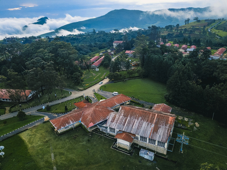 Aerial view of buildings with rusty red roofs contrasting lush green landscapes and dense forests with misty mountains in the distance Obudu Cross River Nigeria.