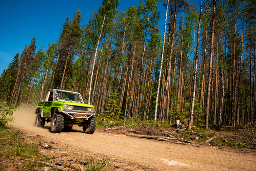 View of a green off road vehicle driving on a dirt road through a dense pine forest near Lake Ladoga in Sortavala Respublika Kareliya Russia.