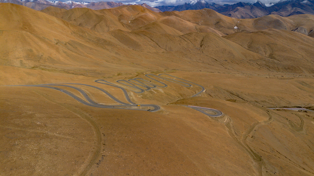 Aerial view of the winding serpentine road at Gawula pass surrounded by arid mountain slopes and distant snow capped peaks in Shigatse Tibet China.