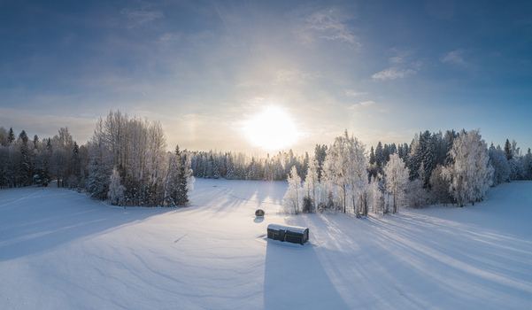 Aerial view of a snow covered landscape with frost covered trees and a small dark structure under a bright winter sun Latvia. Aerial view of a snow covered landscape with frost covered trees and a small dark structure under a bright winter sun Latvia.