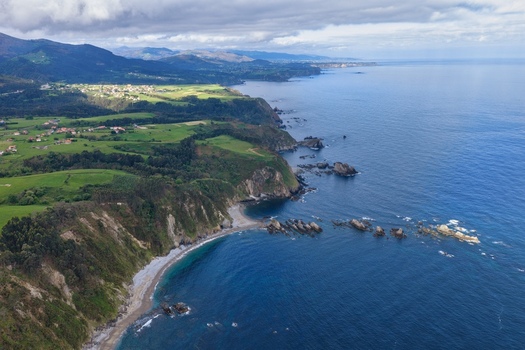Aerial view of Silence Beach Viewpoint with rugged cliffs a pebble beach and turquoise sea along the green coastline of Cudillero Asturias Spain.