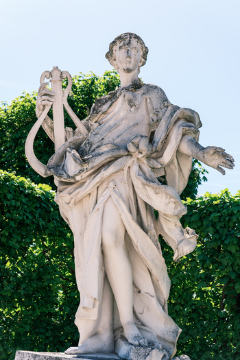 View of a classical stone statue holding a lyre in the gardens of Belvedere Palace with green hedges and blue sky in Vienna Austria. View of a classical stone statue holding a lyre in the gardens of Belvedere Palace with green hedges and blue sky in Vienna Austria.
