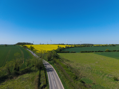Aerial view of New Albion Wind Farm with yellow rapeseed fields and a winding road under a clear blue sky in Rushton England United Kingdom. Aerial view of New Albion Wind Farm with yellow rapeseed fields and a winding road under a clear blue sky in Rushton England United Kingdom.