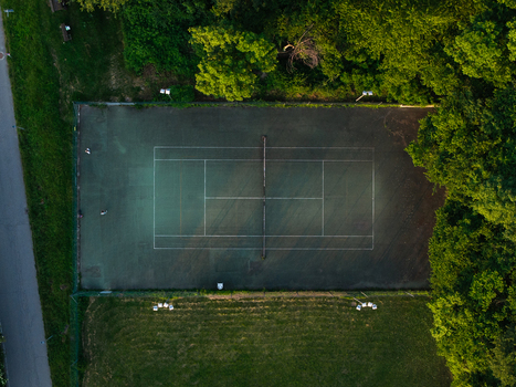 Aerial view of a green tennis court surrounded by dense green trees and a grassy field during the golden hour Chiusa di San Michele Piemonte Italy.