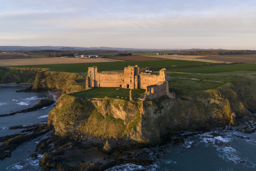 Aerial view of Tantallon Castle ruins on a high cliff overlooking the North Sea with golden sunlight on the stone walls and green fields North Berwick Scotland United Kingdom.