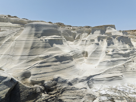 Aerial view of the white volcanic rock formations of Sarakiniko beach with smooth textures and deep shadows under a clear blue sky in Milos Greece. Aerial view of the white volcanic rock formations of Sarakiniko beach with smooth textures and deep shadows under a clear blue sky in Milos Greece.
