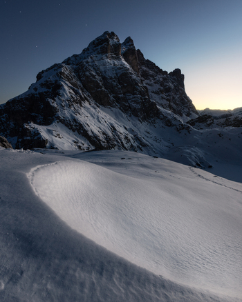 View of the snow covered Dolomites mountain peaks under a twilight sky with stars and textured snow dunes in the foreground Trentino Alto Adige Italy. View of the snow covered Dolomites mountain peaks under a twilight sky with stars and textured snow dunes in the foreground Trentino Alto Adige Italy.