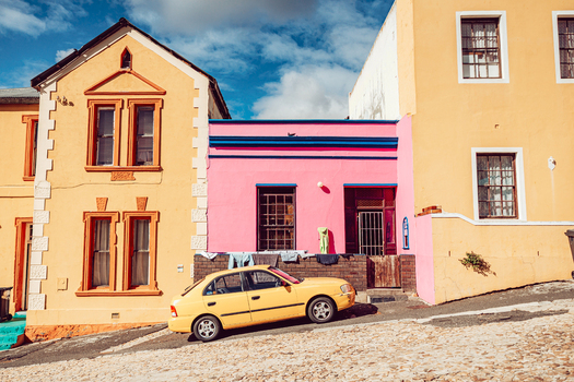 View of colorful pink and yellow houses with a yellow car parked on a steep cobblestone street in the Bo Kaap neighborhood of Cape Town Western Cape South Africa. View of colorful pink and yellow houses with a yellow car parked on a steep cobblestone street in the Bo Kaap neighborhood of Cape Town Western Cape South Africa.
