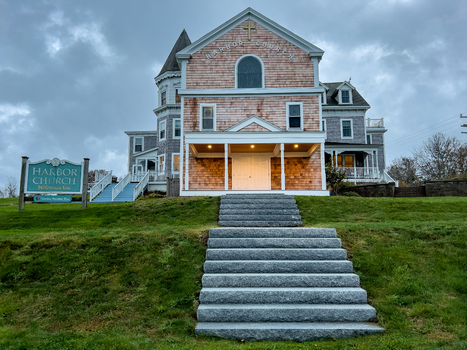 View of the Harbor Church on Block Island with its shingled facade stone steps and a sign in the foreground under a cloudy sky in New Shoreham Rhode Island United States.